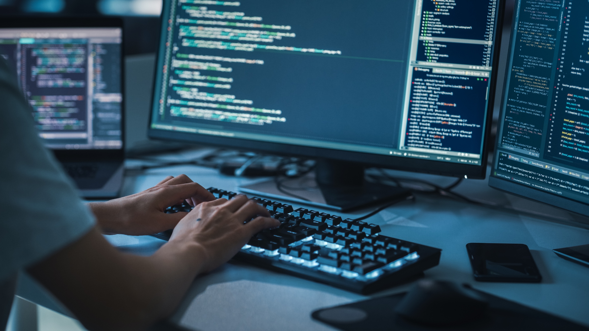 A developer working at a keyboard with code on multiple monitors