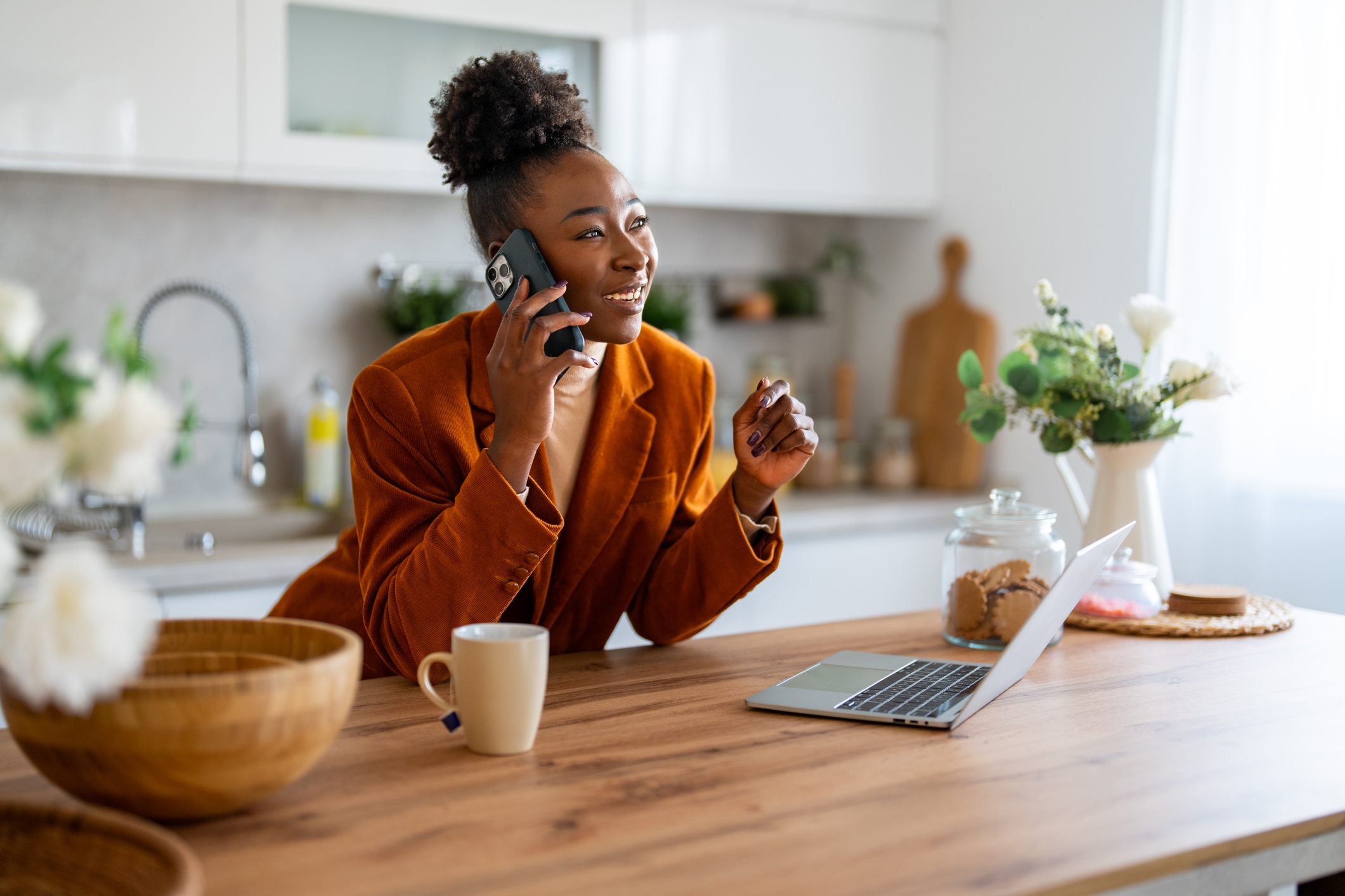 A woman talking on a mobile phone beside her laptop at home